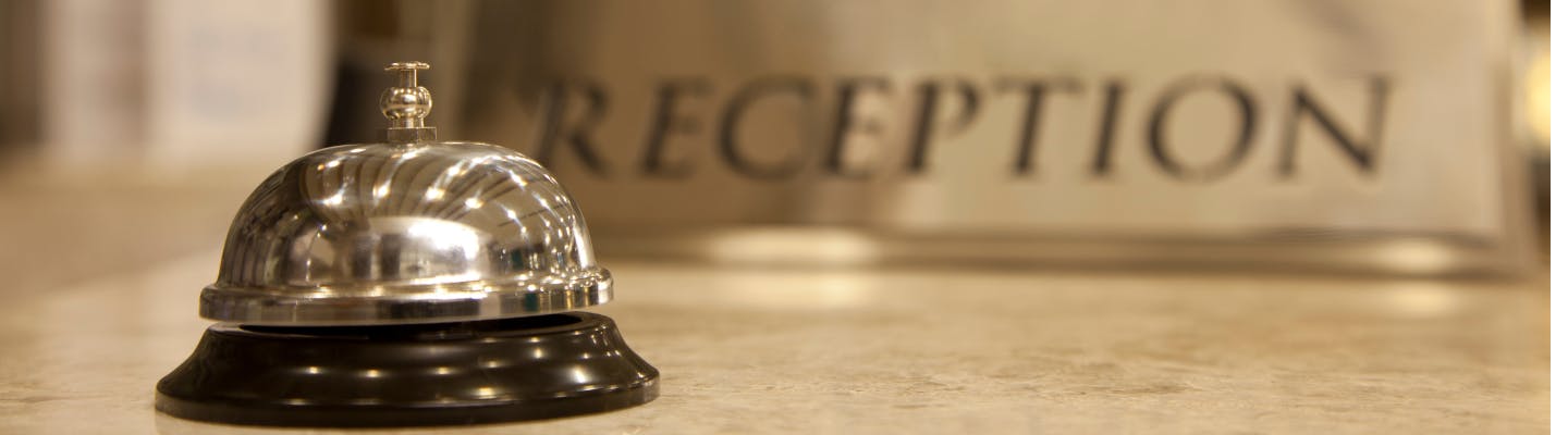 A service bell at the front desk of a hotel with a sign in the background that reads "reception"