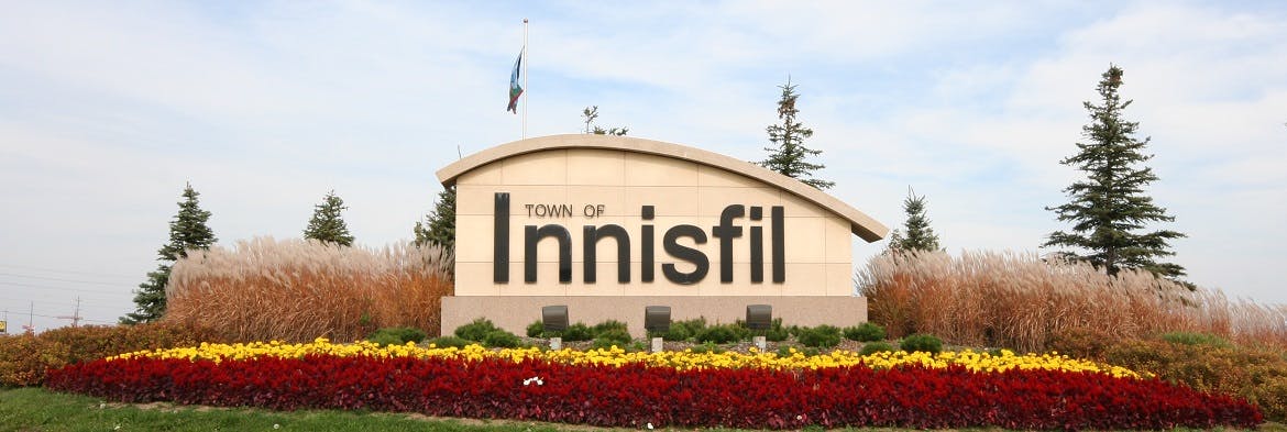 Innisfil Town Entrance installation showing the Name of a concrete struction with flowers in the foreground and grasses and trees in the backgroun