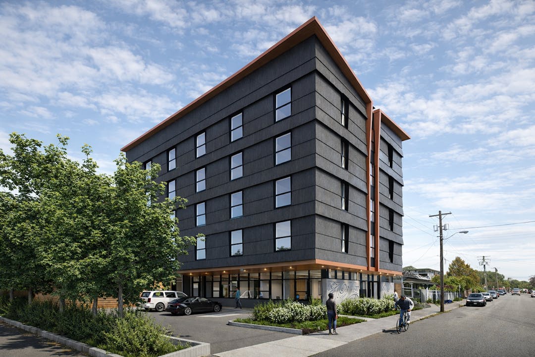 Six-story modern apartment building with dark facade and wood accents on a quiet street, with trees, cars, and cyclists.