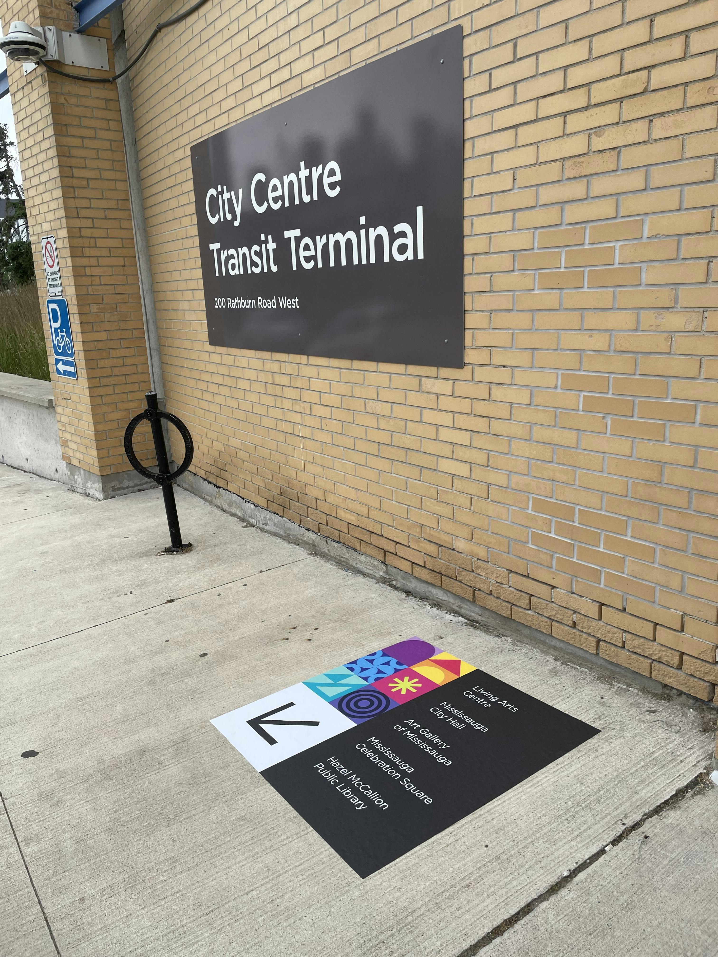Signage for City Centre Transit Terminal on a brick wall, with directional information on the pavement guiding to nearby locations.