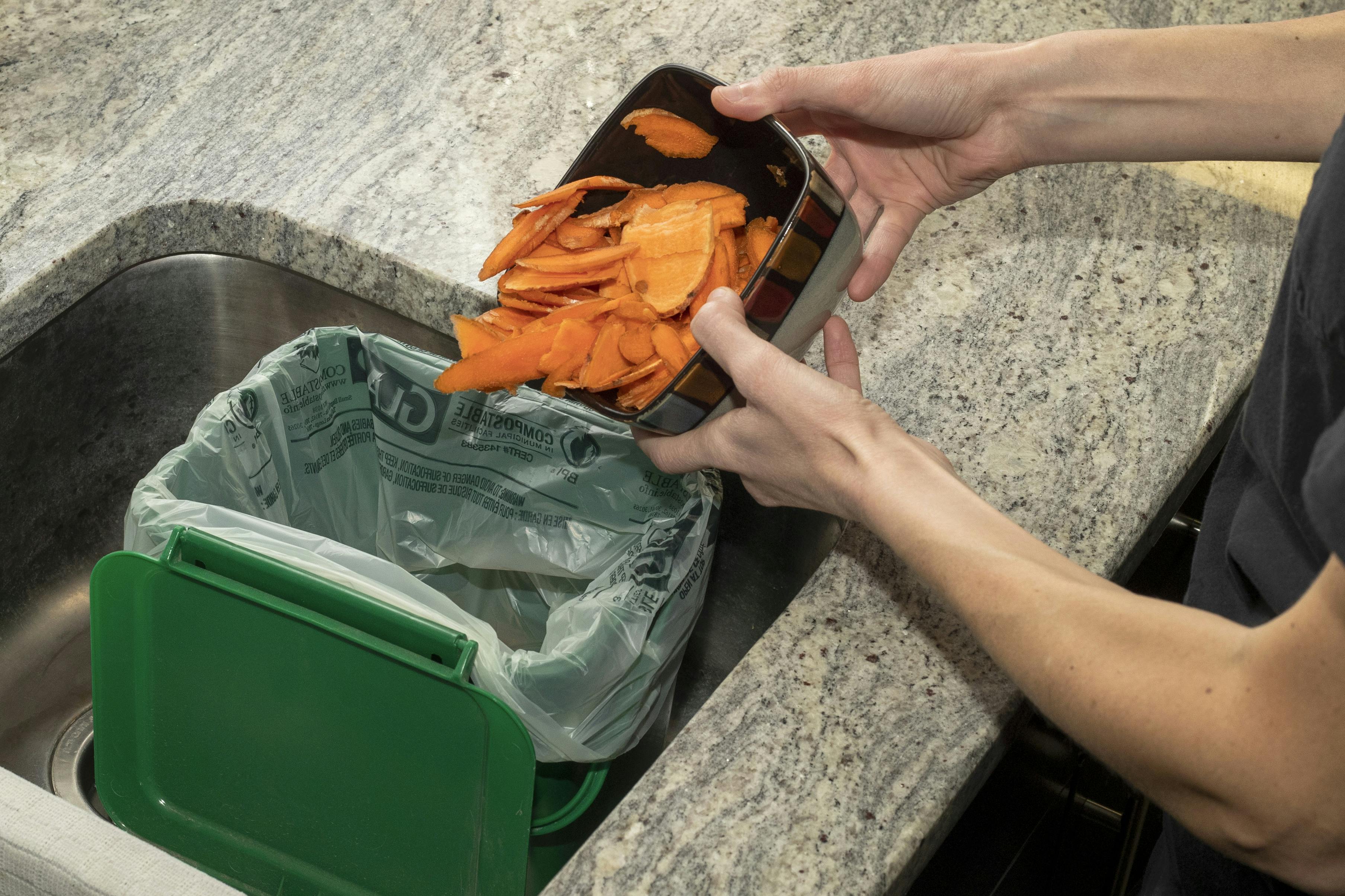 Organic materials like vegetable skins being placed in the kitchen container