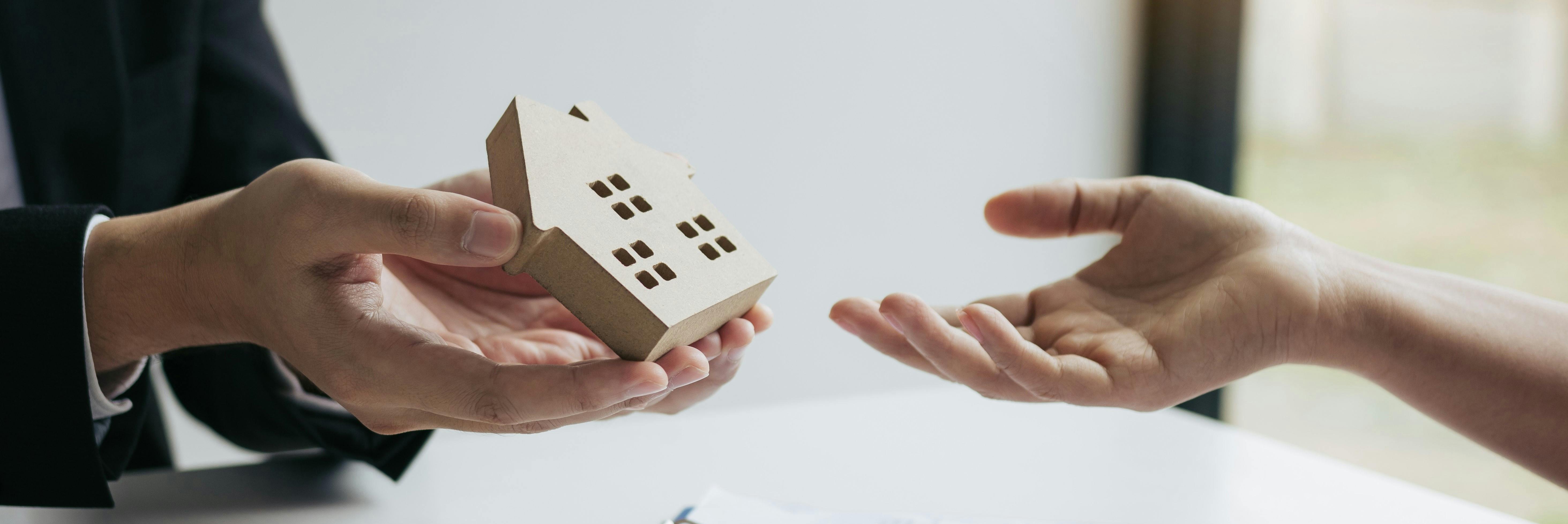 A hand holding a small wooden house 