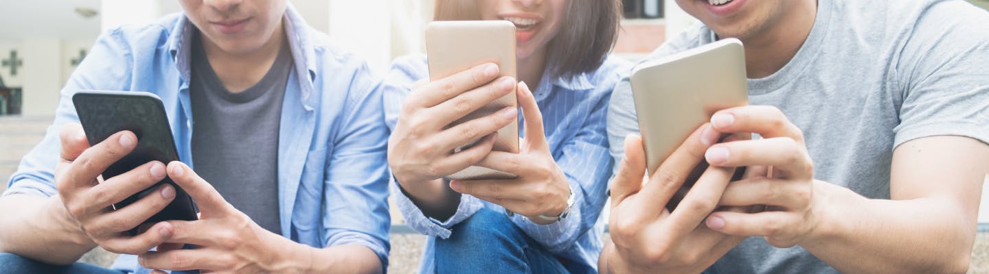 Three young adults sit outside checking their mobile devices