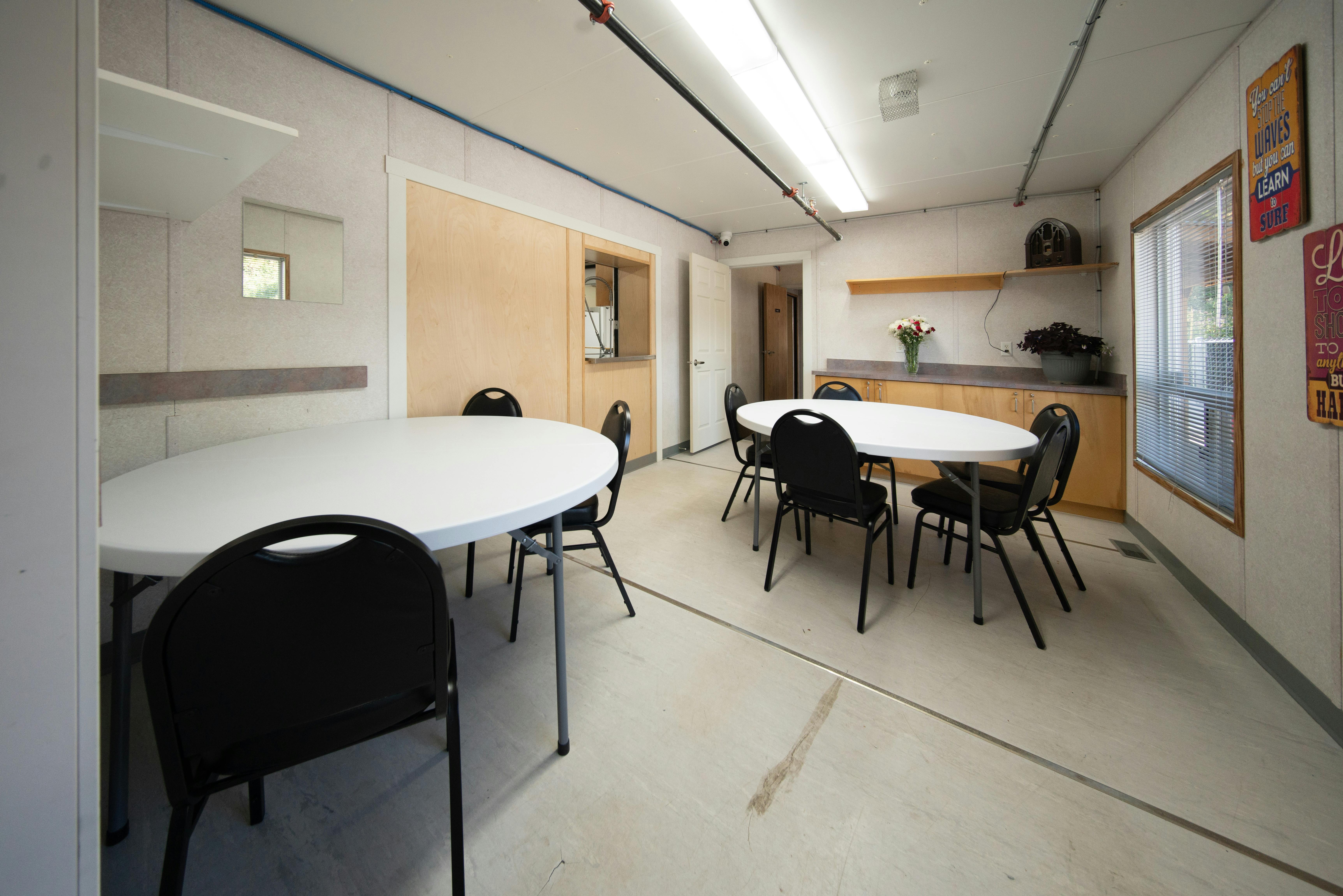 Meeting room with two round tables, black chairs, white walls, soundproof panels, grey carpet, bulletin board.