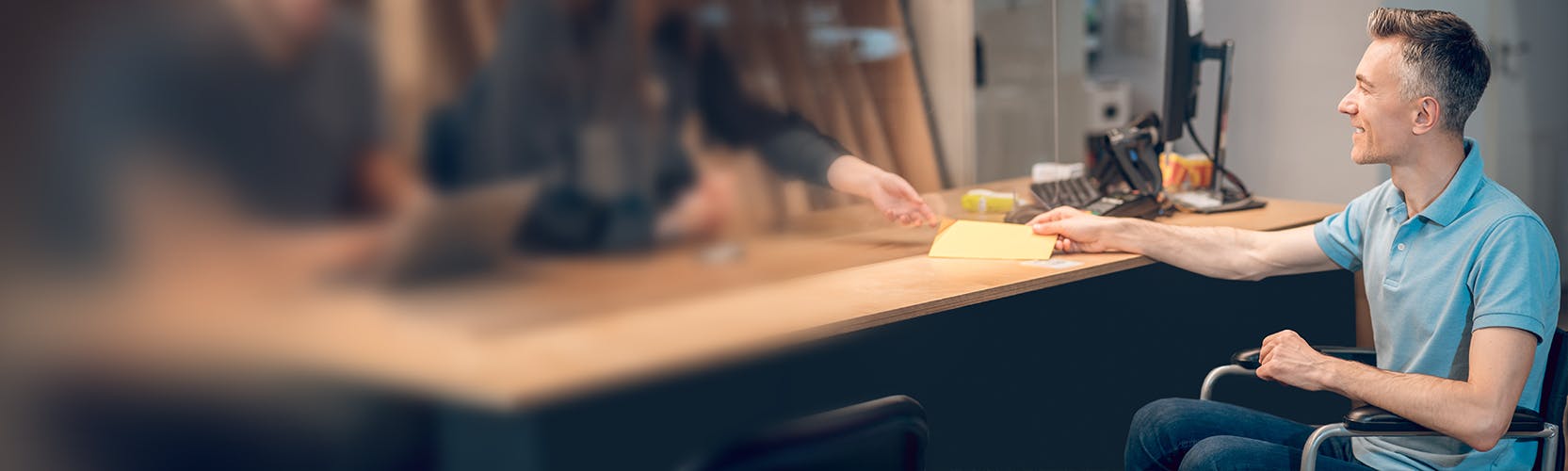 a man in a wheelchair handing off a paper to an employee behind a desk