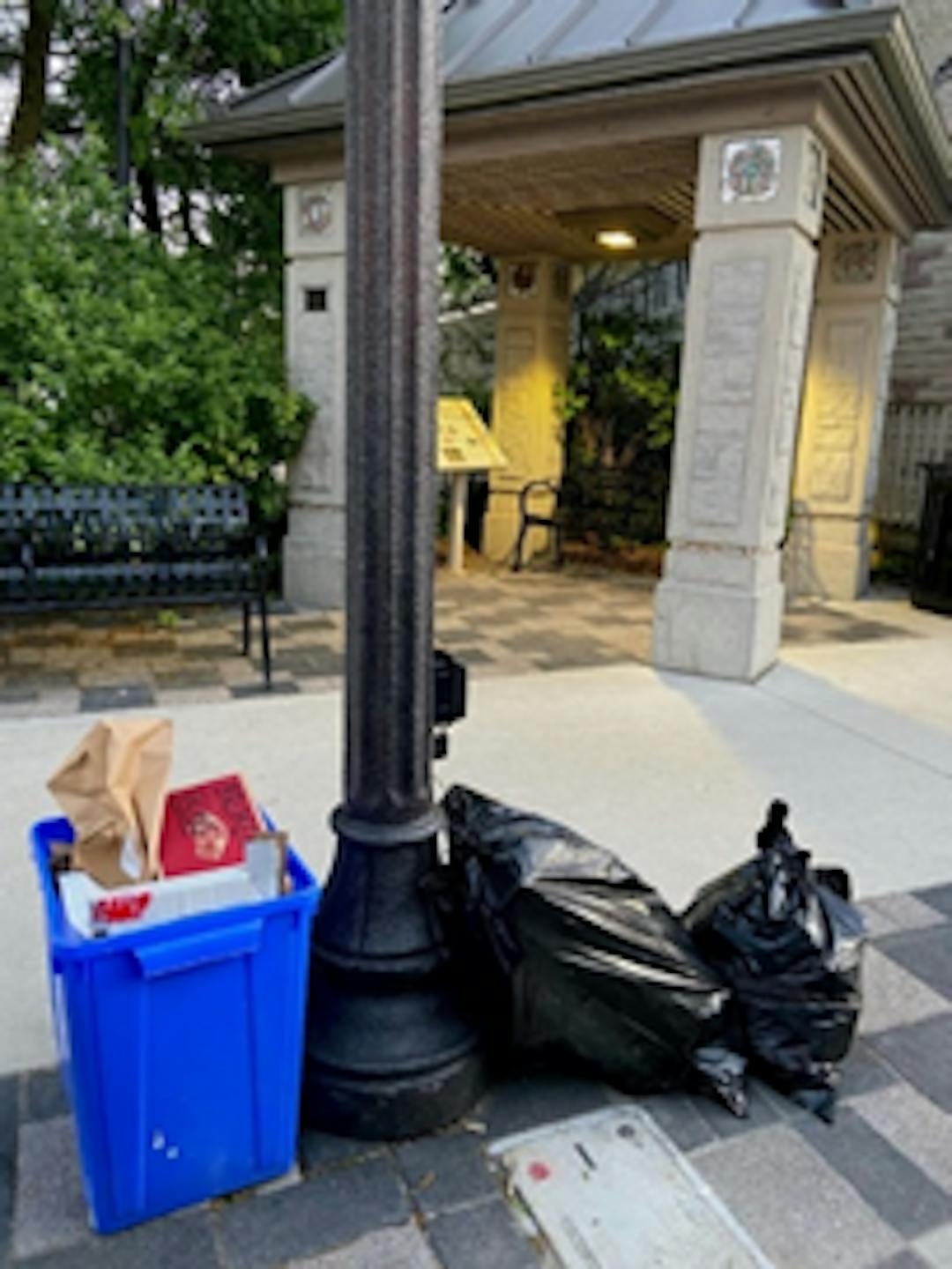 a blue box and two black garbage bags lying next to a street light along the curb