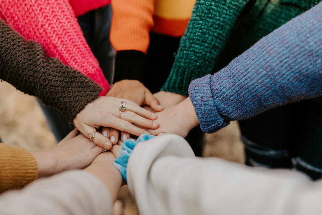 Image is of many hands that are brown and white and overlapping each other. Some hands have rings and bracelets.