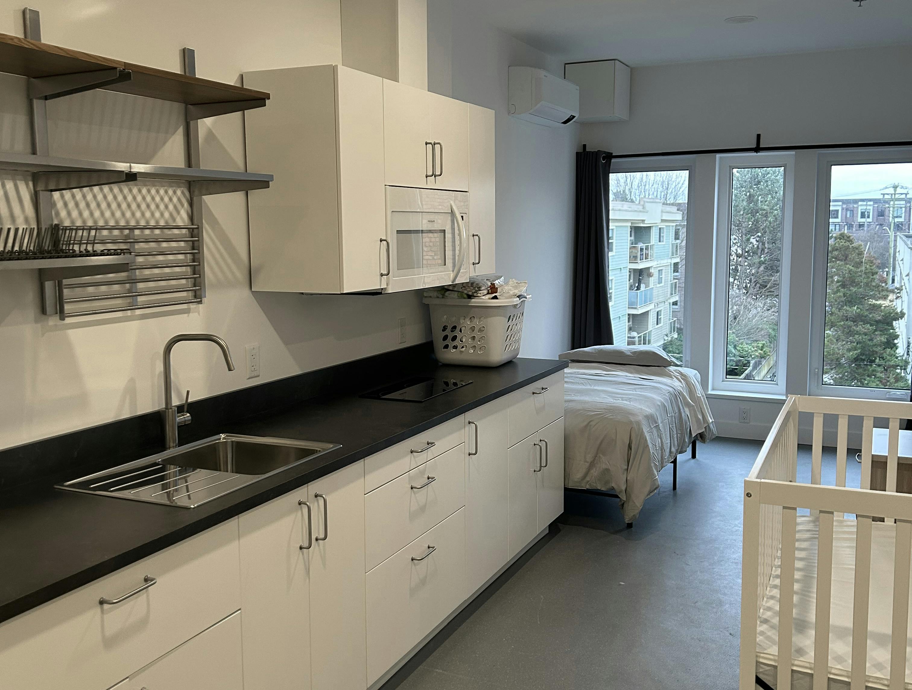 A modern, compact studio apartment with a kitchenette, a single bed, and a crib.