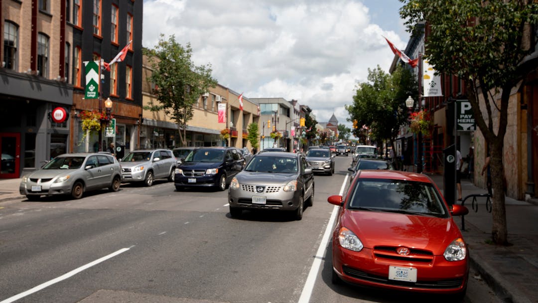Cars parked along George Street while vehicles drive by, in downtown Peterborough