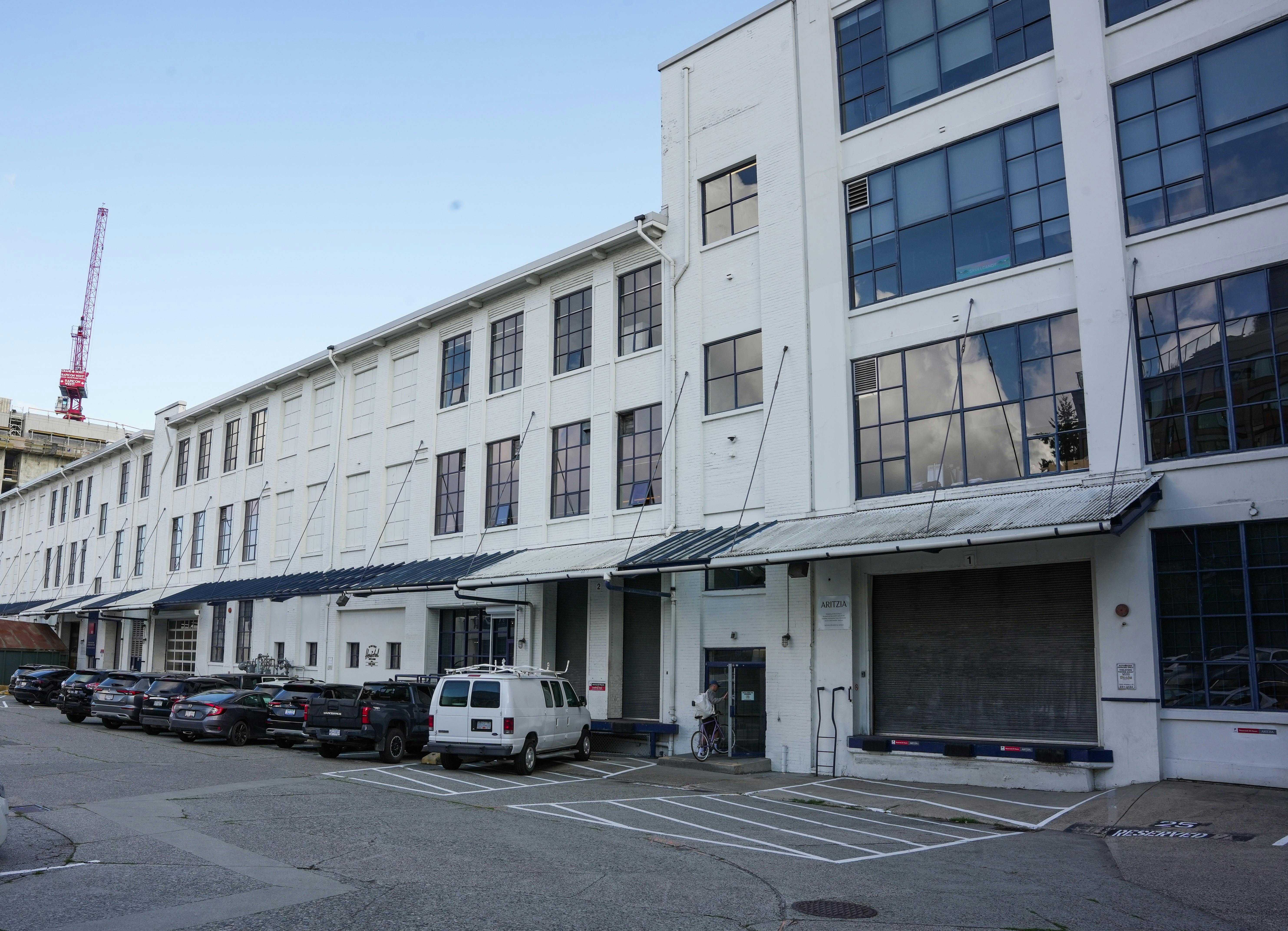 White multi-story industrial building at with large grid-style windows and metal awnings.