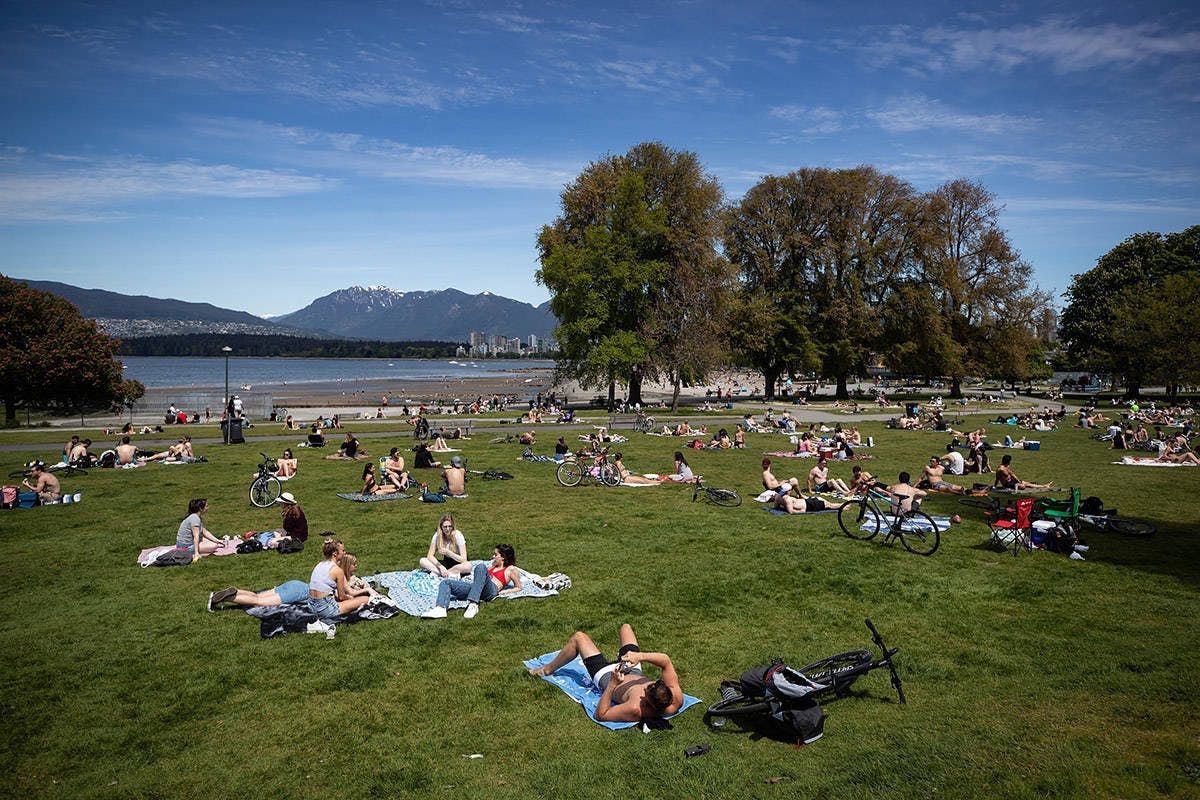 People on blankets at Kits Beach park on a sunny day with the ocean and mountains in the background
