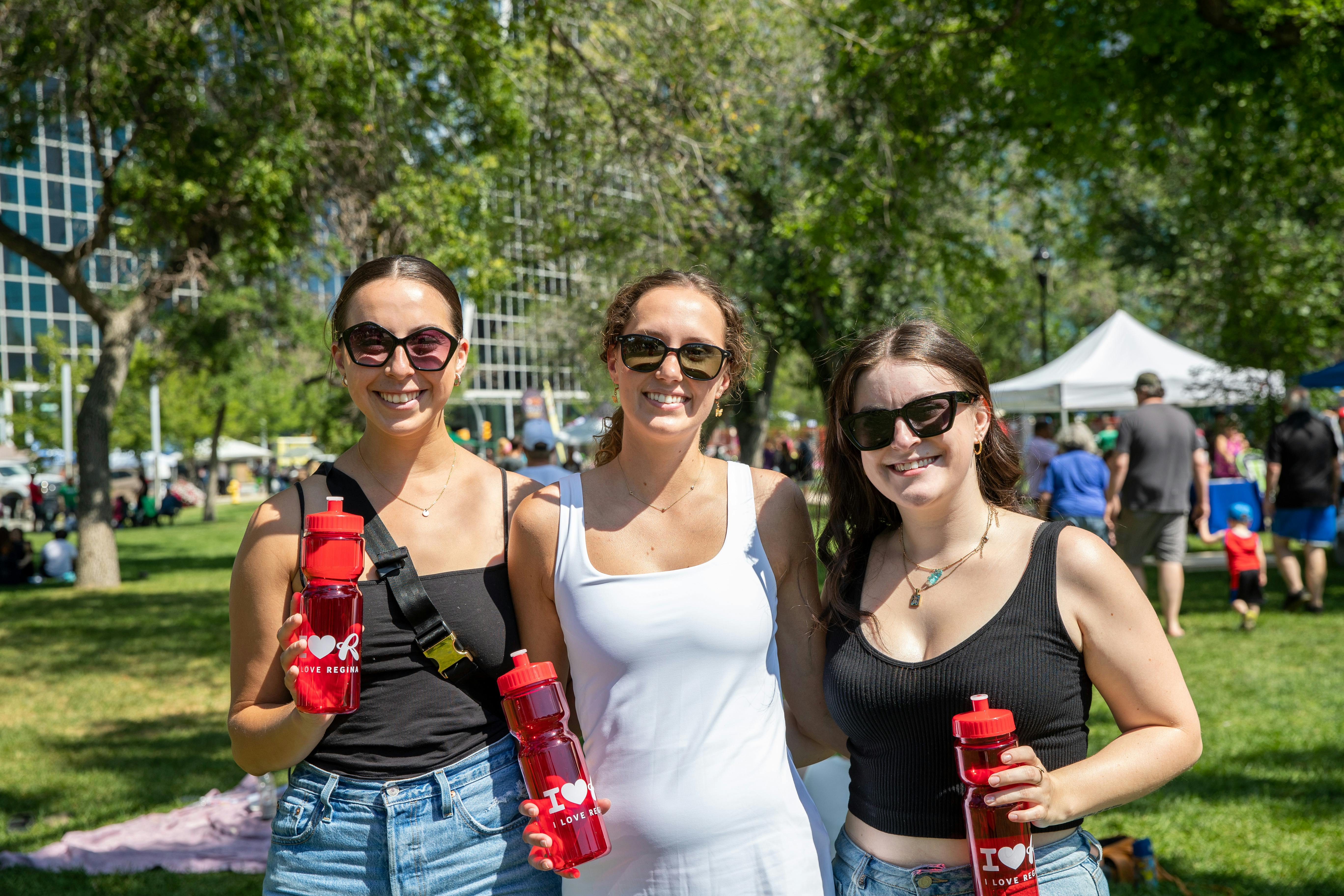 Three young women in sunglasses smile for a photo in Victoria Park during I Love Regina Day.