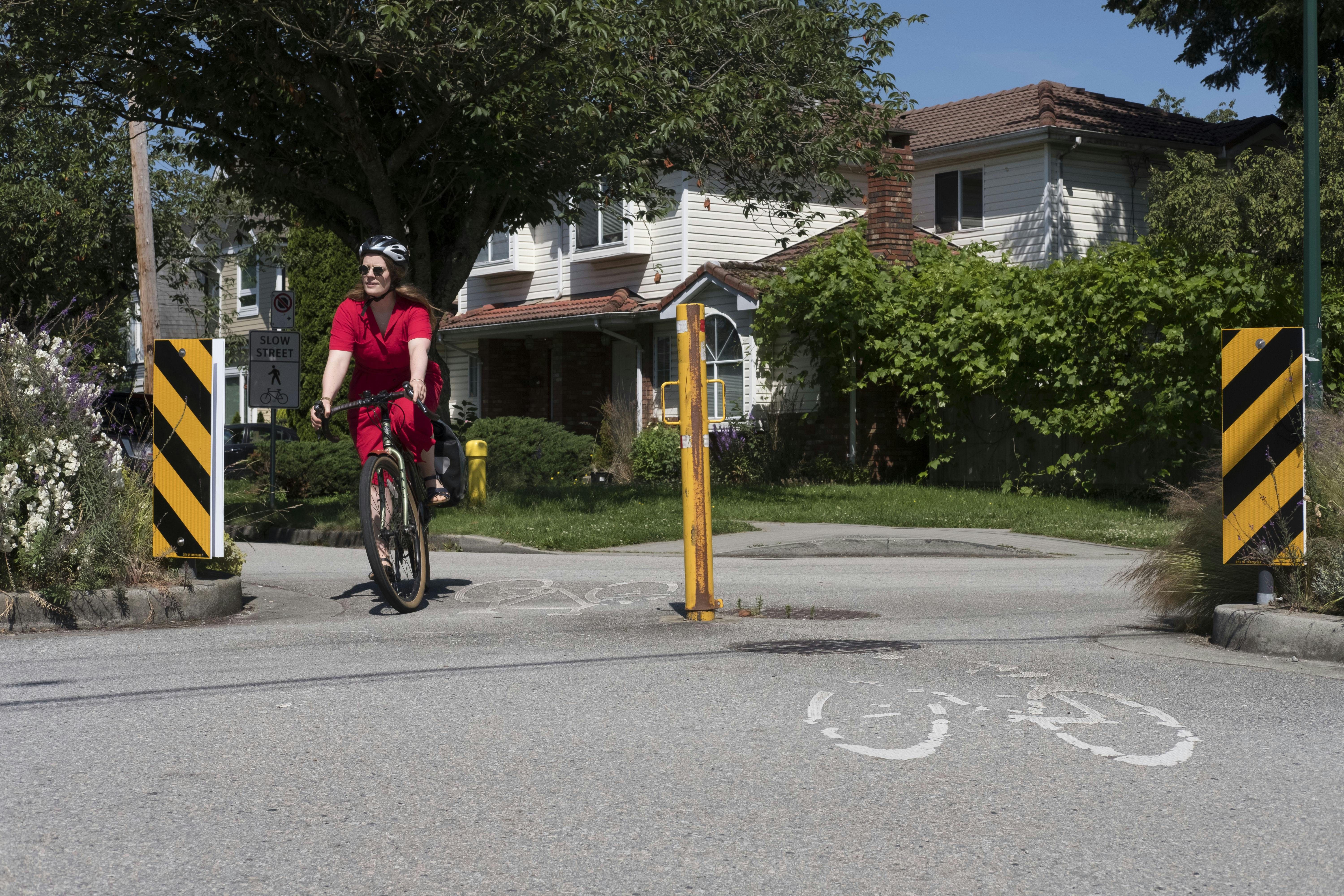 A cyclist in a red dress cycling along Slow Streets - Charles St at Lakewood Dr. Slow Streets connect neighbouring parks and open spaces.