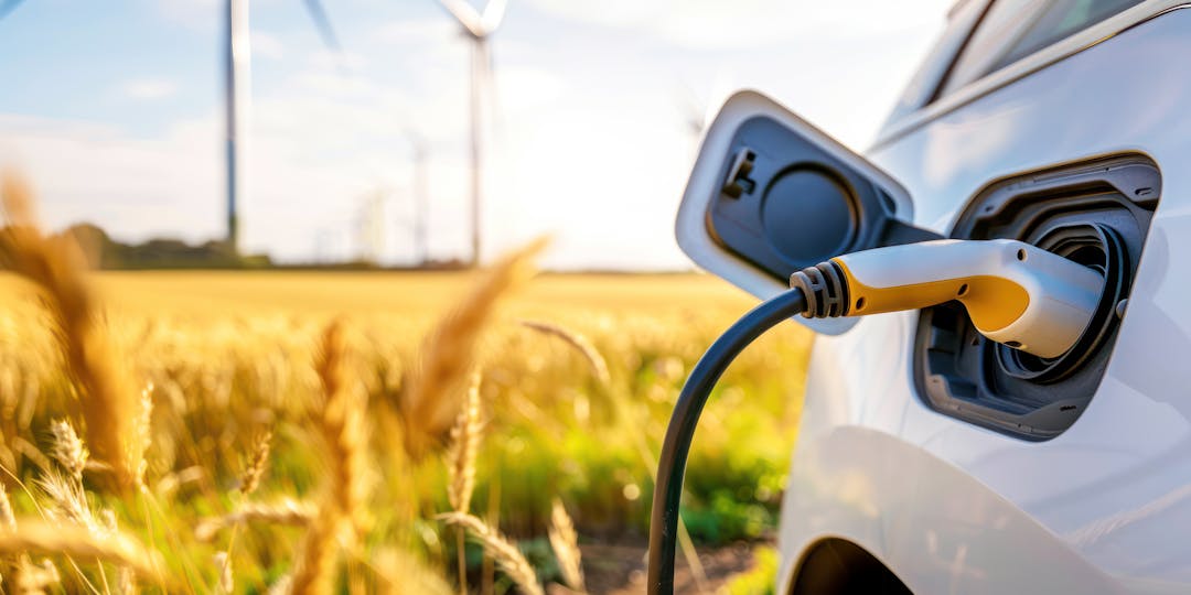 Electric vehicle charging next to a farm field with wind turbines in landscape