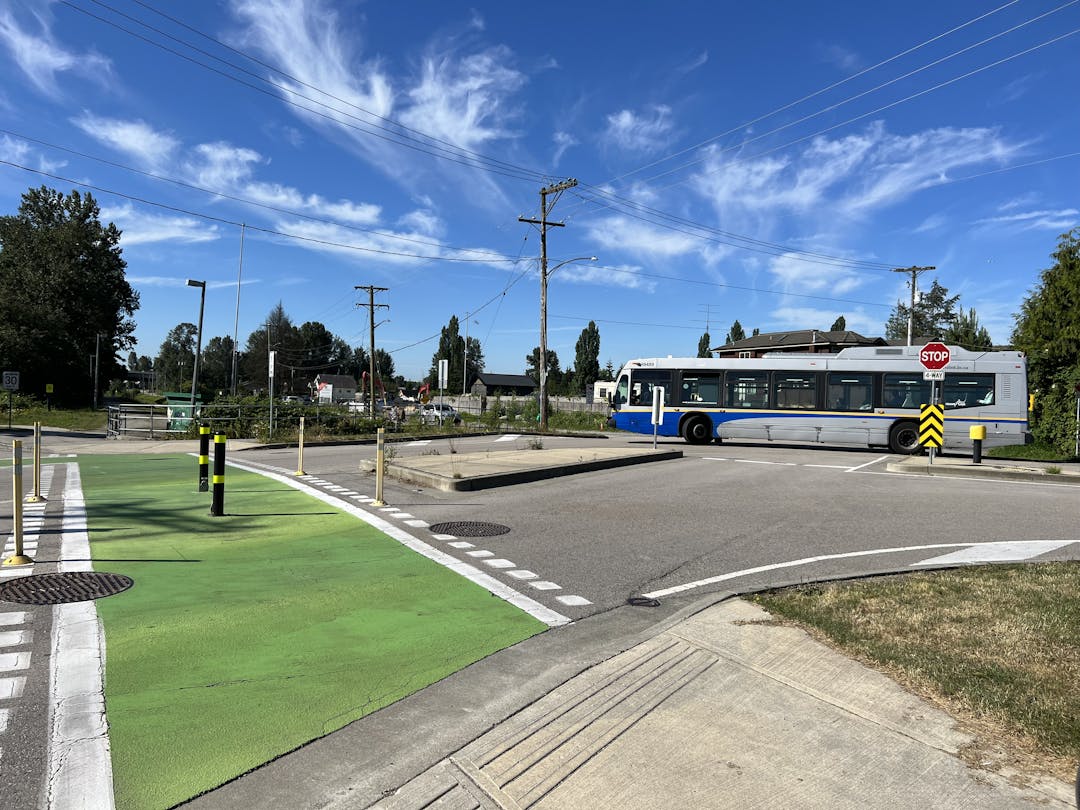 An intersection in Queensborough with a crosswalk, bike lane with green paint on the pavement, and Translink bus. 
