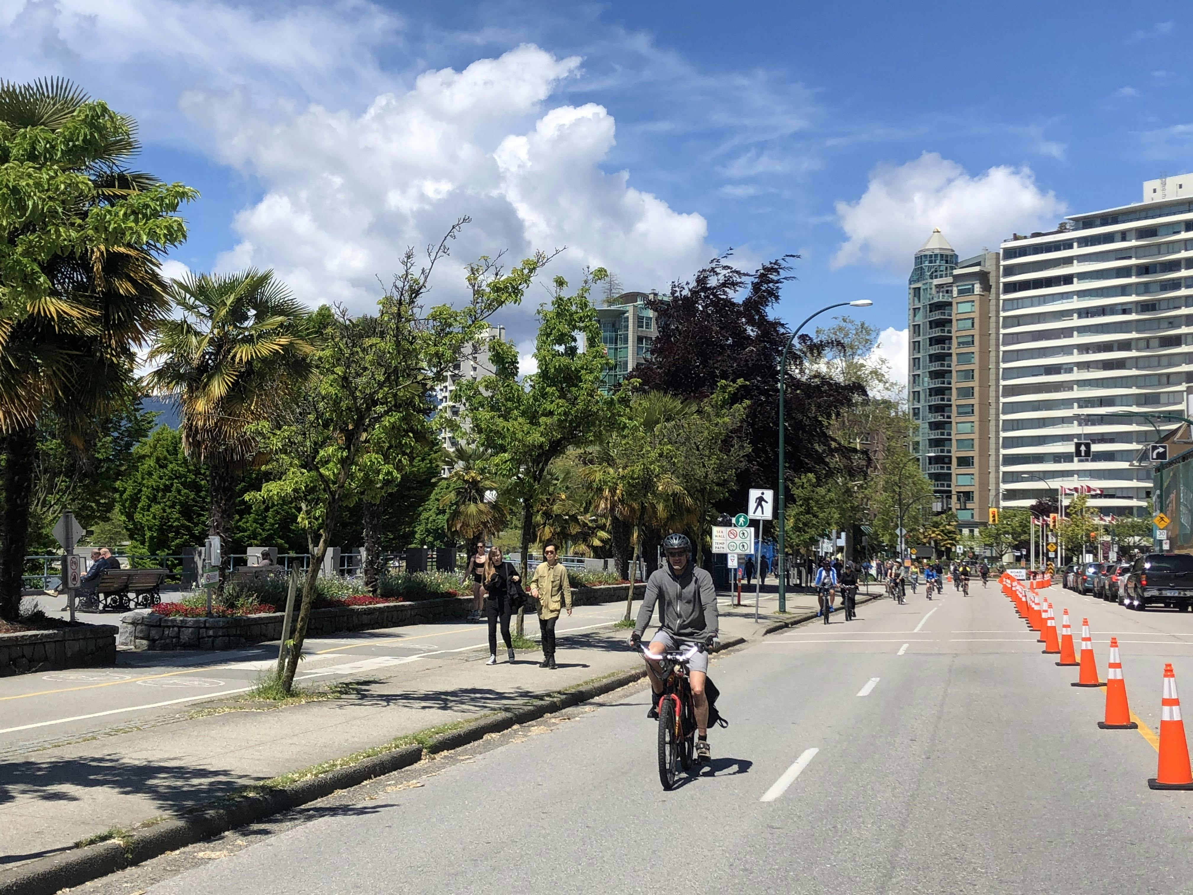 People walking on the sidewalk, people cycling on the road in the Room to Move area on Beach Avenue