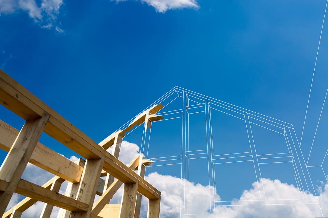 Unfinished wood frame of a building in the foreground with blue sky and clouds in the background.