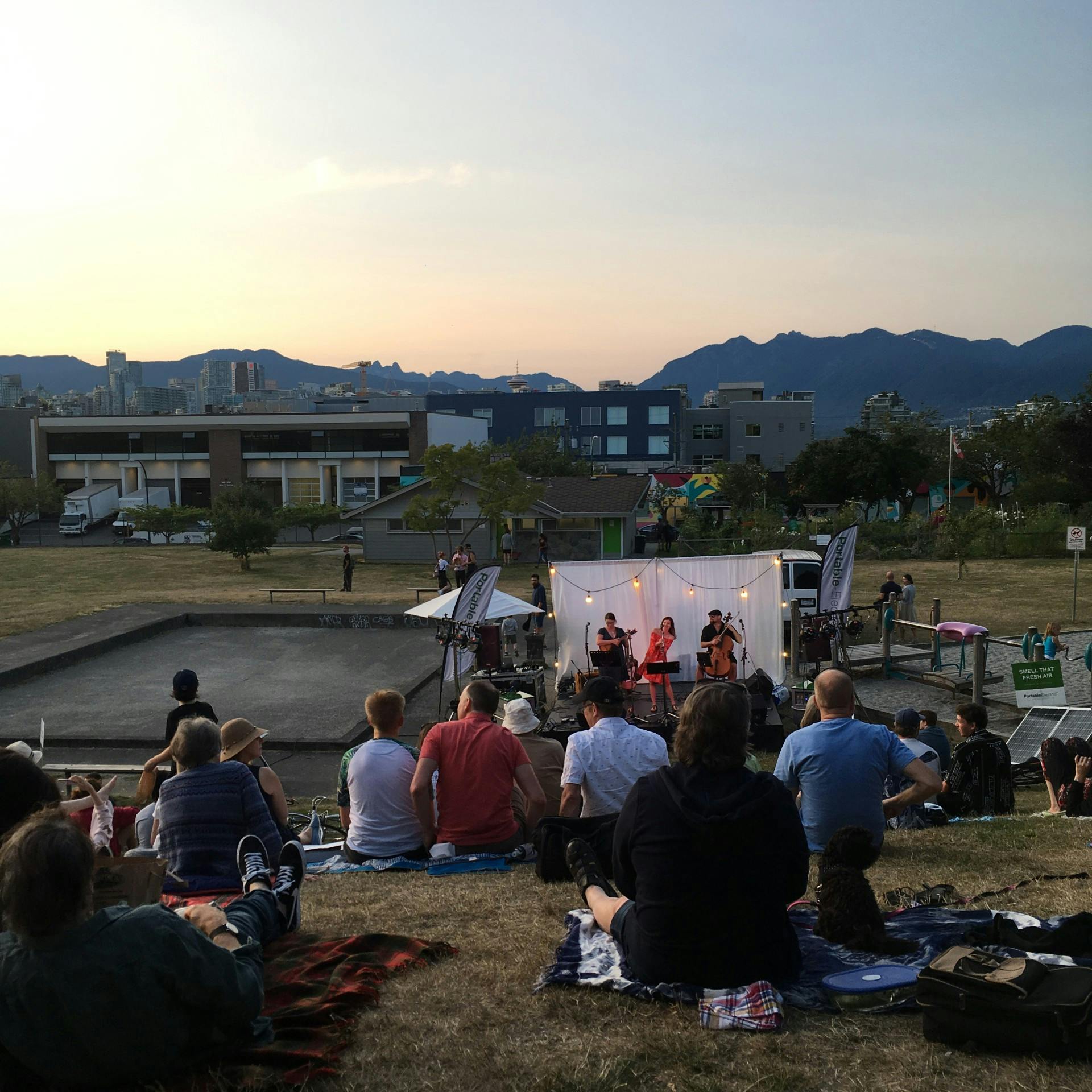 Band performing in front of a white screen with a crowd seated on the slope