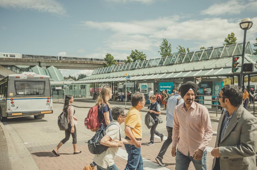 Passengers milling about at the Surrey Central bus loop on a sunny summer day