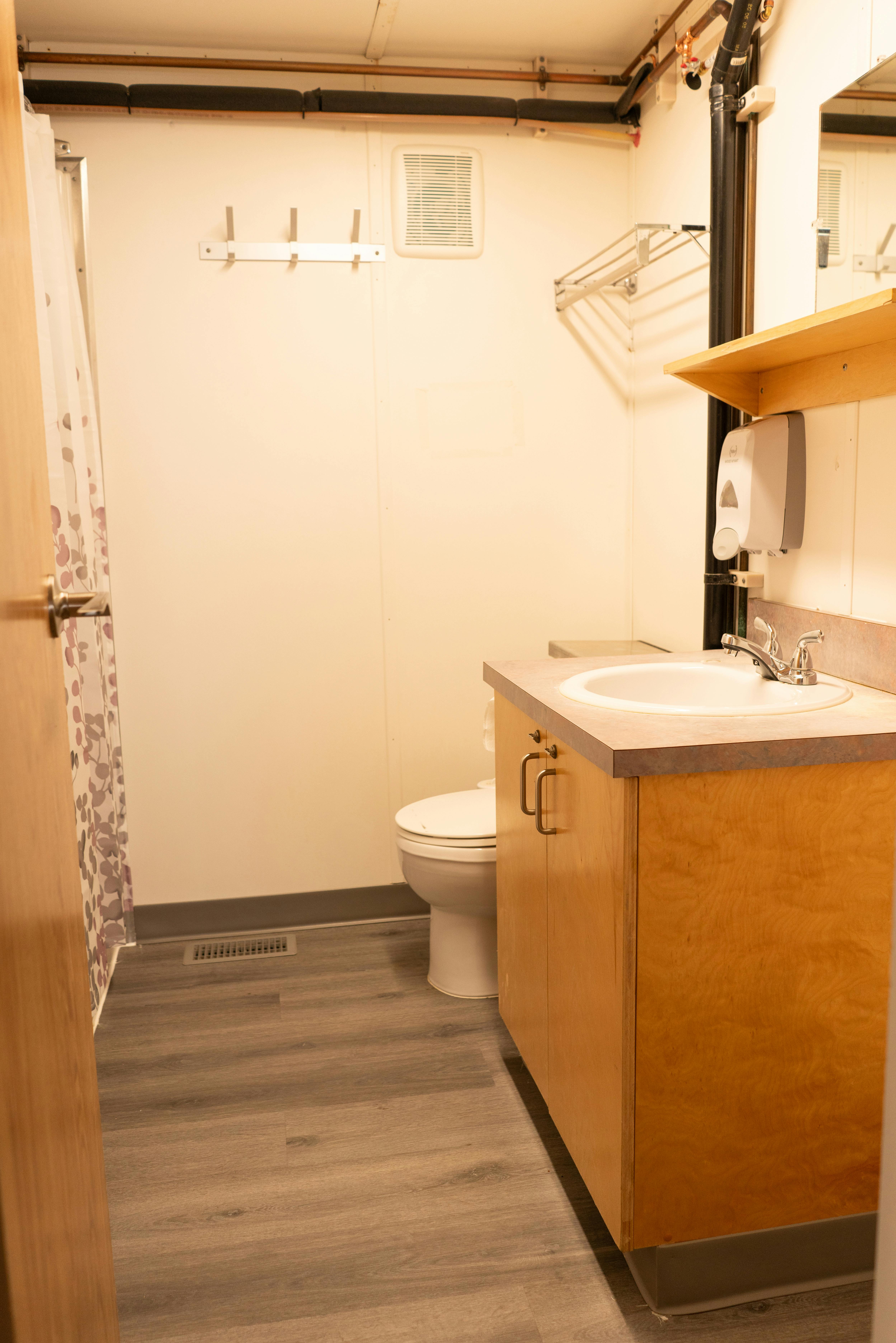 Commercial kitchen with stainless steel appliances, wooden cabinets, marble-like countertops, grey wood-like floor.