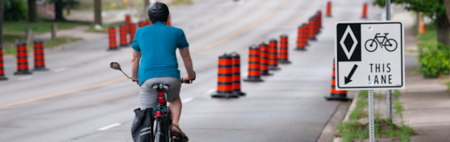 Cyclist driving on road in expanded bike lane with large construction pylons used as barrier. 