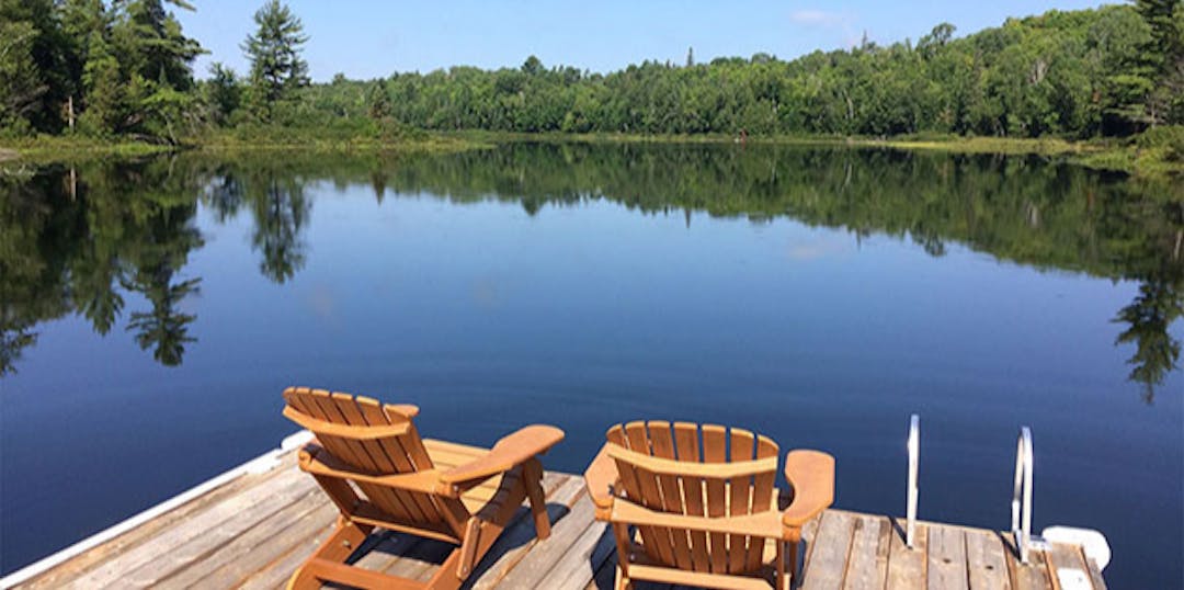 two muskoka chairs on dock overlooking glassy water