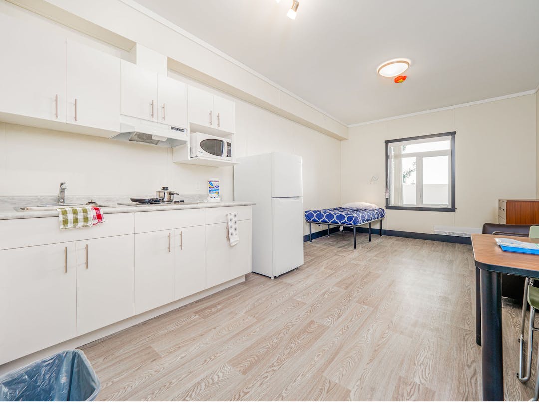 A unit in a supportive housing building, with a white kitchen and furniture.