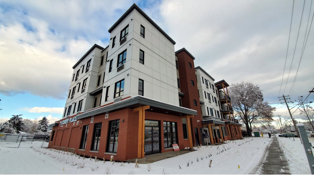 Exterior photo of new three-storey supportive housing building. Street view with snow.