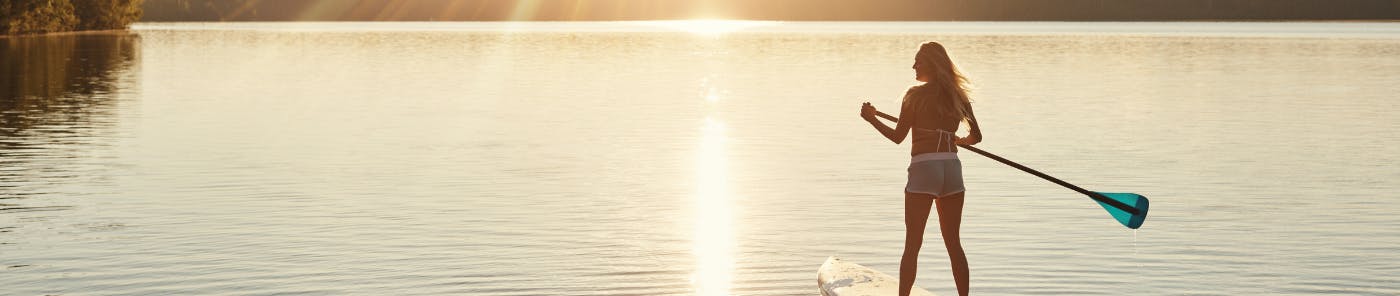 Woman stand up paddle boarding at sunset