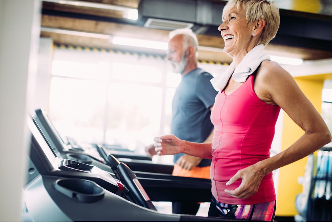 Senior woman in foreground on treadmill. Senior man in background on treadmill.