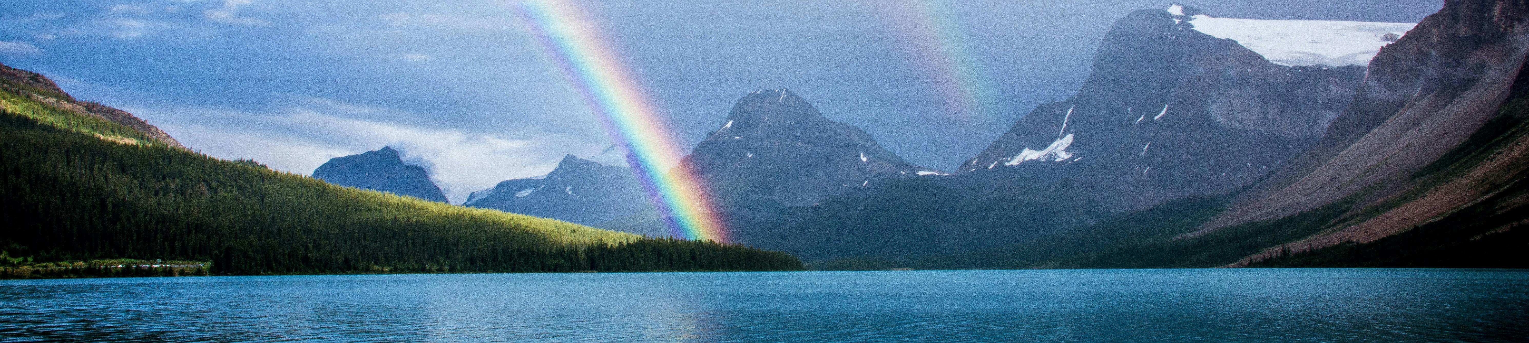 view over the lake showing two rainbows and snow touched mountains.