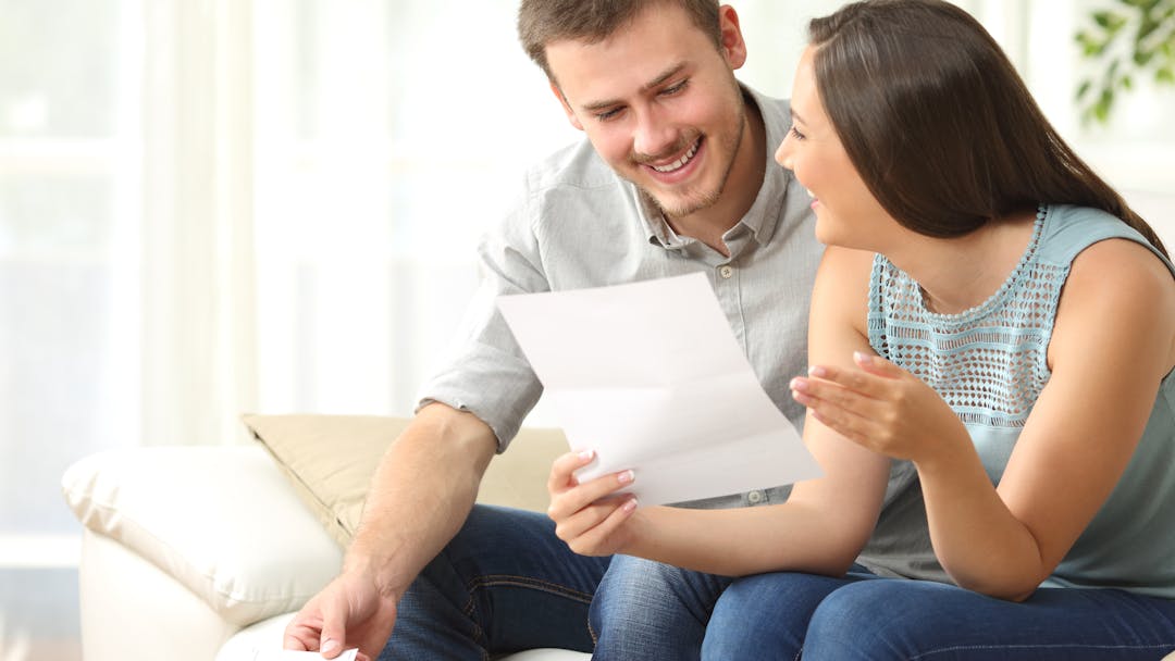 A woman and man sitting on a couch looking at a piece of paper with a calculator on the coffee table