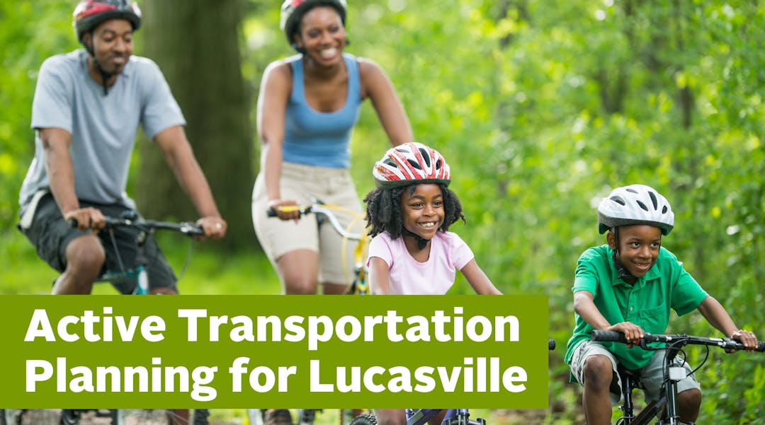 a photo of a family of four riding bikes in he summer surrounded by trees. 