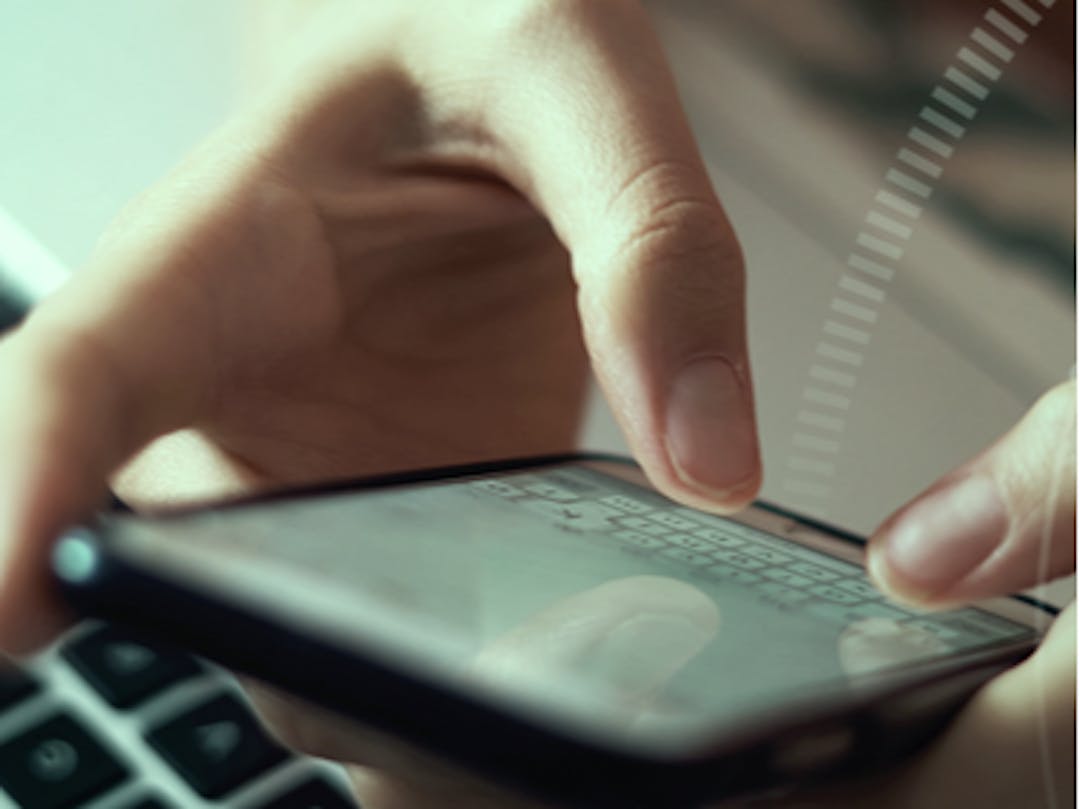 Hands typing on cellphone with laptop in background 