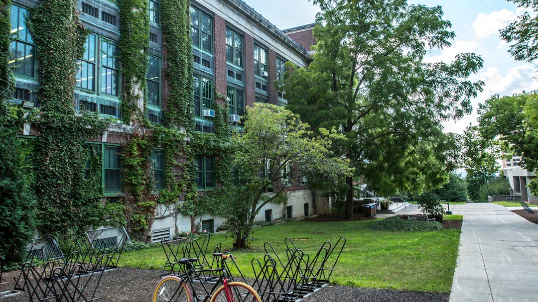 three story brick building covered in vines, with a path and bicycle rack in front