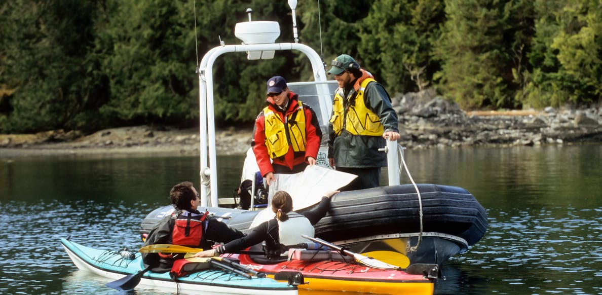 Parks Canada wardens in an inflatable patrol boat review a marine charter with two sea kayakers in Pacific Rim National Park