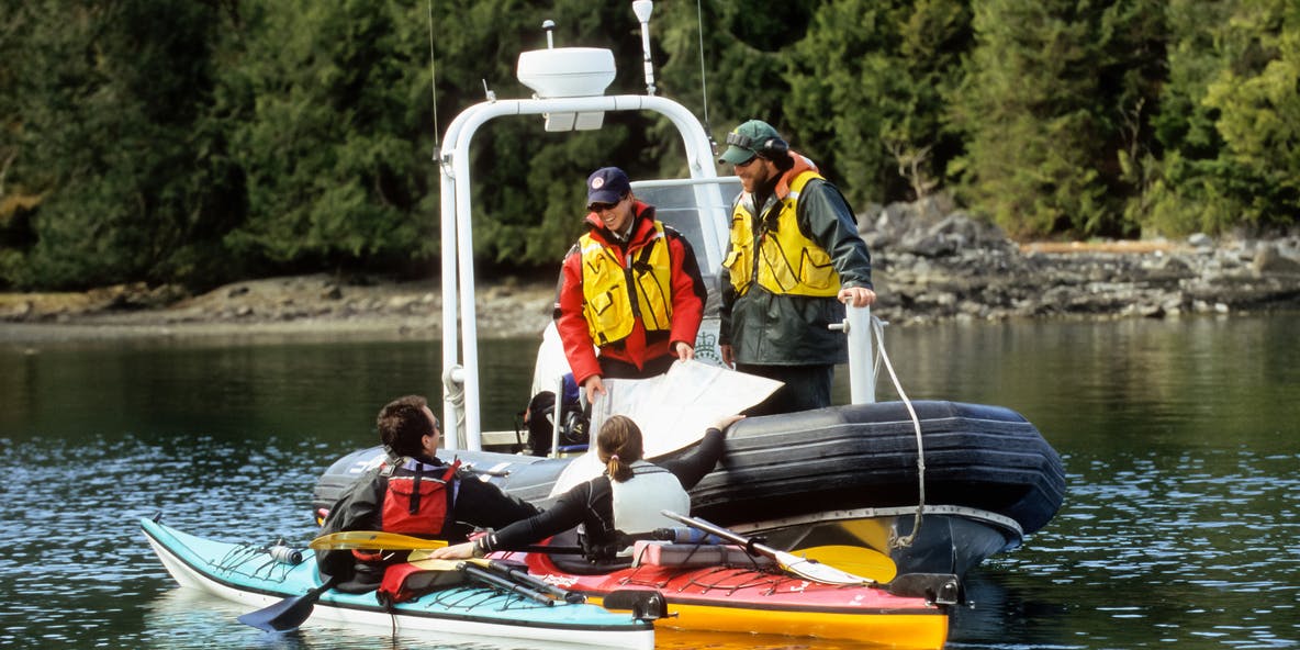 Deux gardes de parcs de Parcs Canada à bord d’un bateau gonflable examinent une carte marine avec deux kayakistes de mer