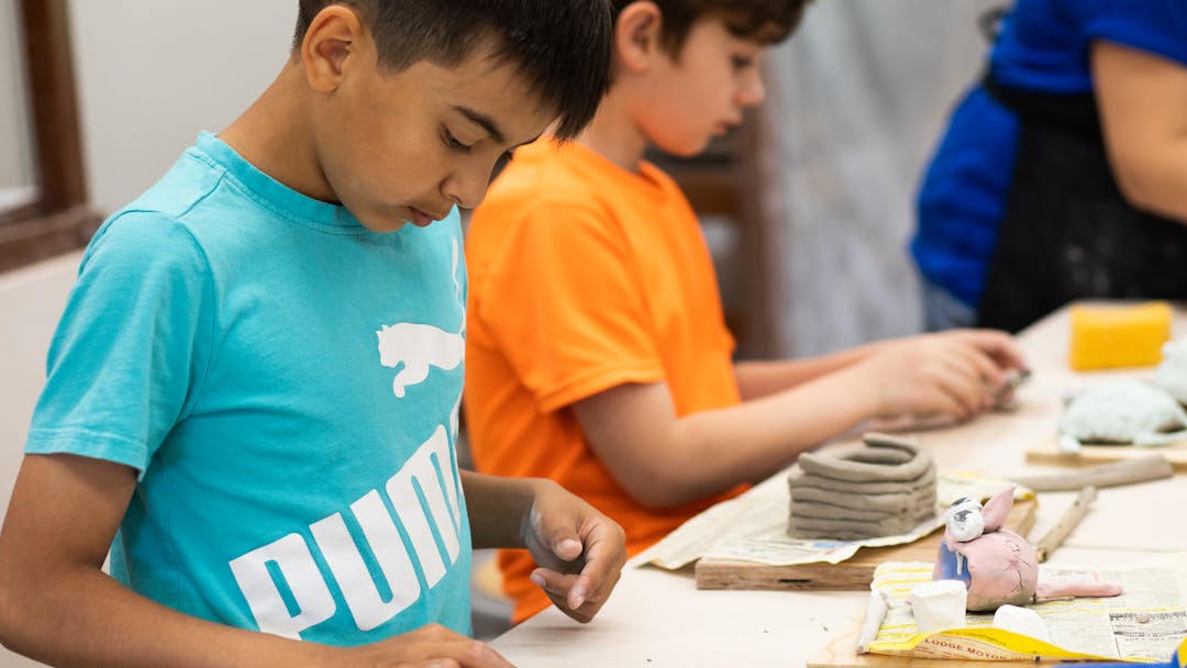 Child in an pottery class flattening out some clay.