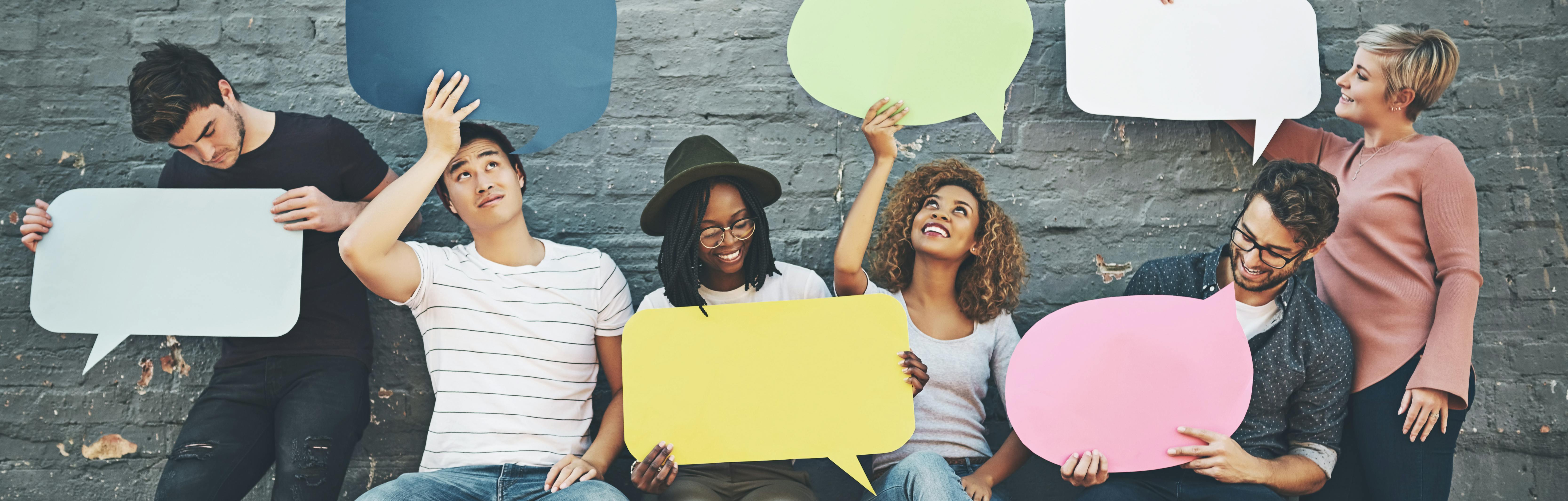 Six young adults against a brick wall holding up speech bubbles and enjoying the conversation.