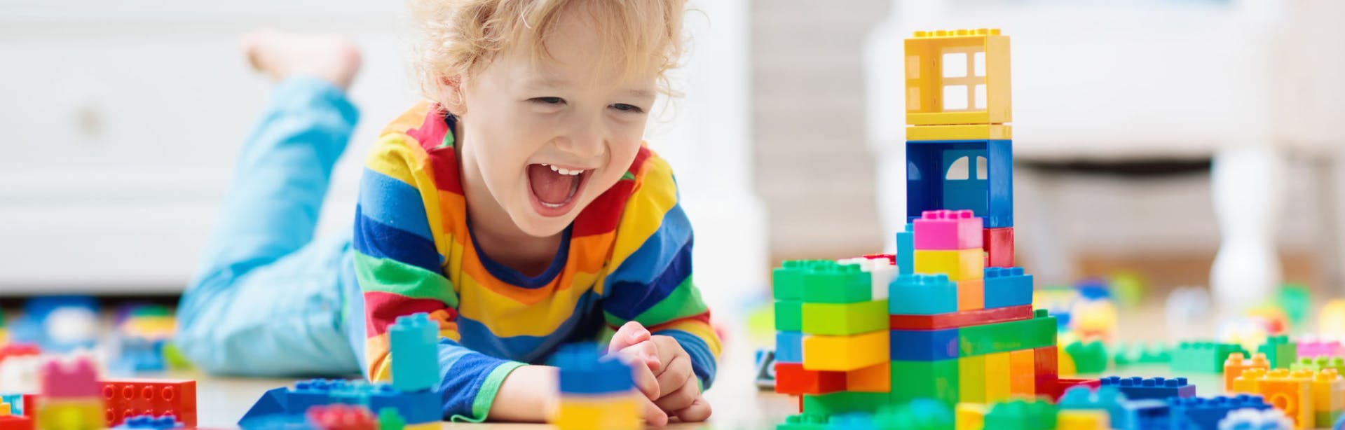 Young child lays on stomach, laughing while playing with building blocks on the floor