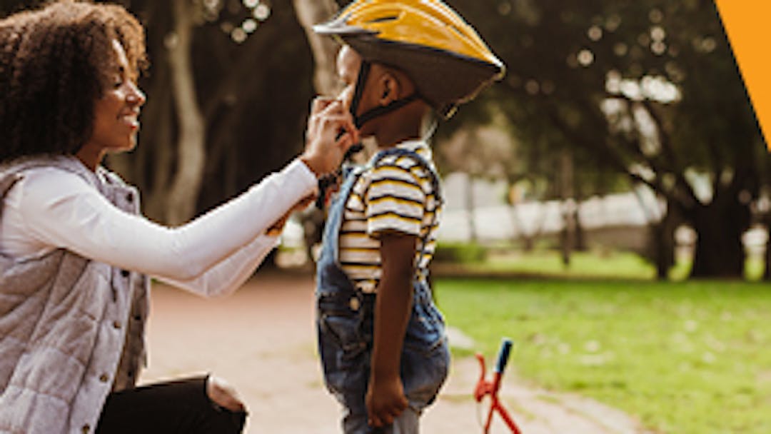 A woman putting a cycling helmet on a child on a shared use path