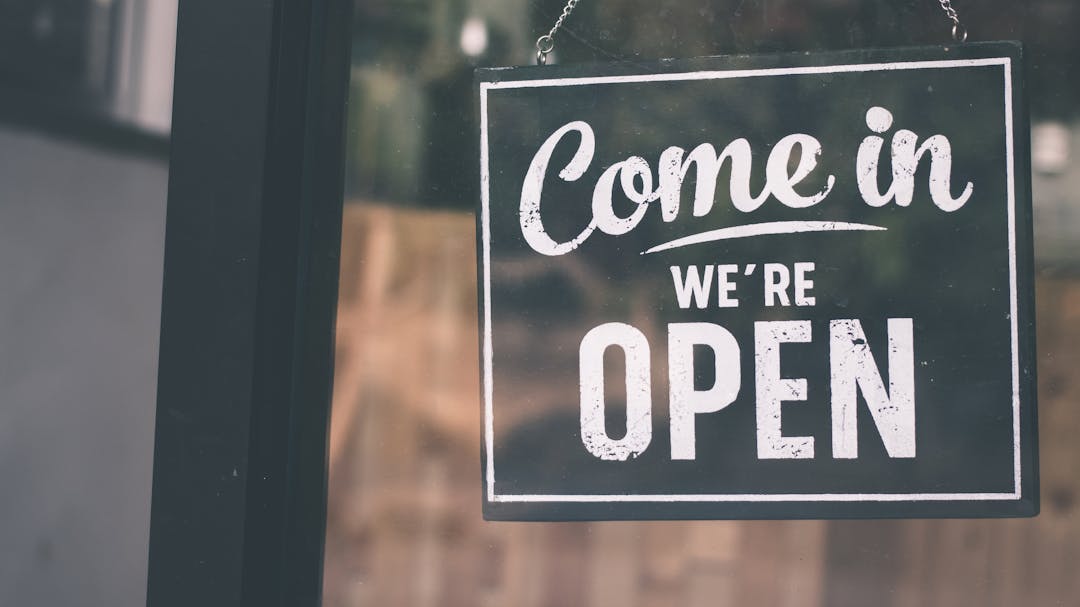 Black sign hanging on a glass door that reads "Come in we're open"