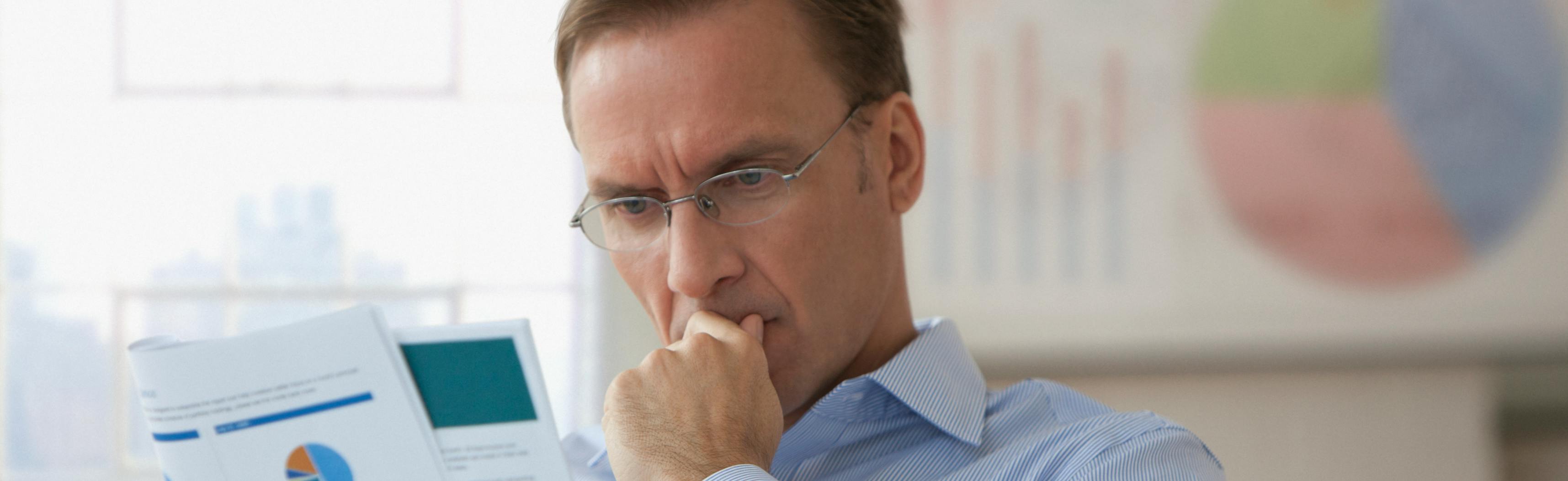 Man reading a business report in an office in front of the window and a chart