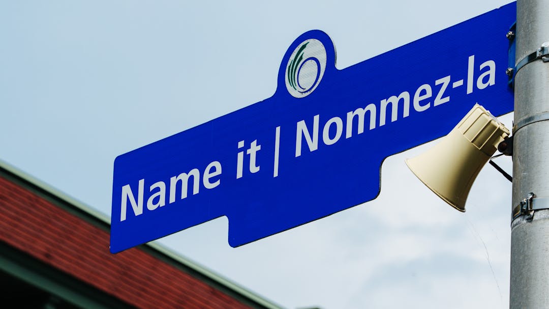 A blue street sign with white font that says 'Name it' and 'Nommez-la'. 