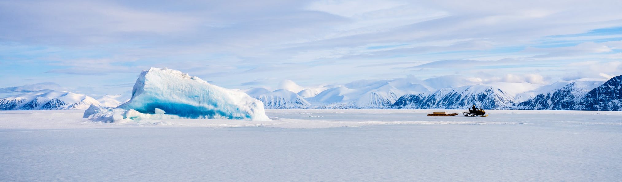 Single snowmobile rider towing cargo on the sea ice terrain of Tallurutiup Imanga National Marine Conservation Area. 