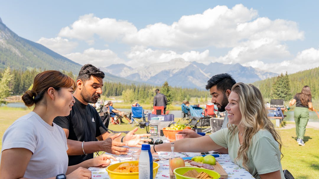 Four people enjoy a picnic on a sunny day with Cascade ponds and mountains in the background. 