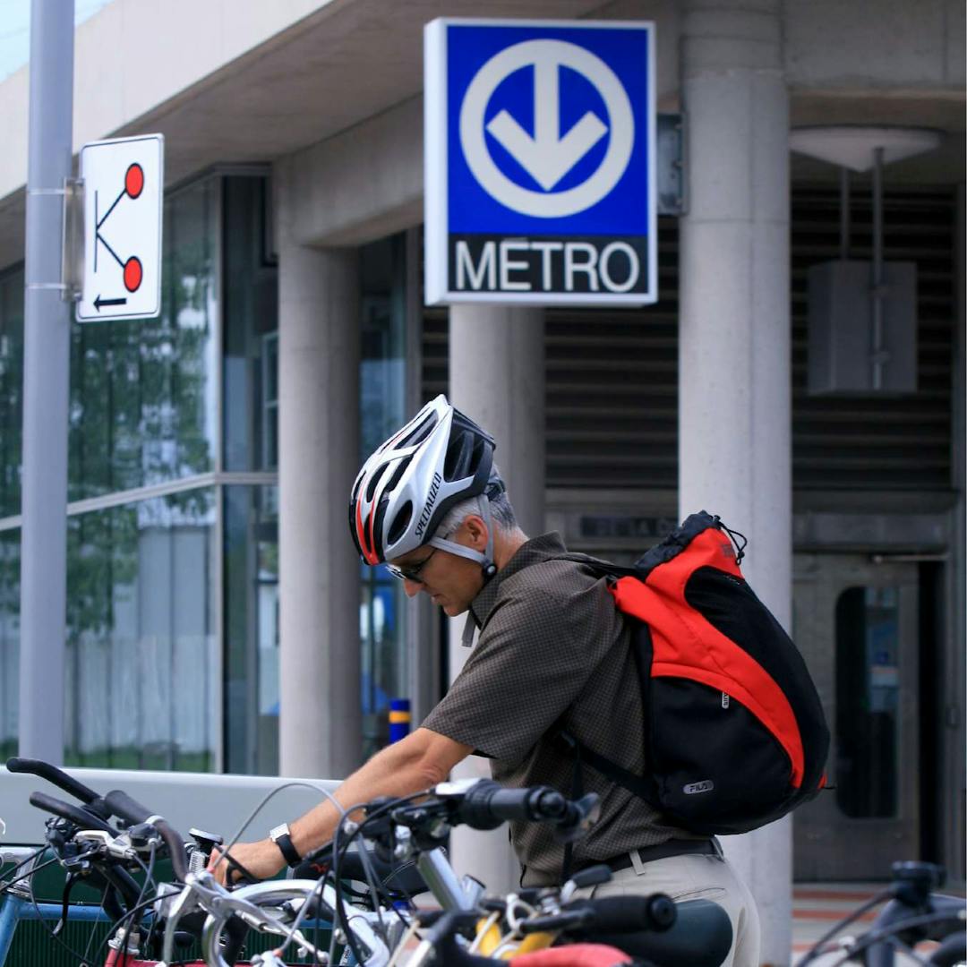 une personne range son vélo dans un rack à vélo devant une entrée de métro