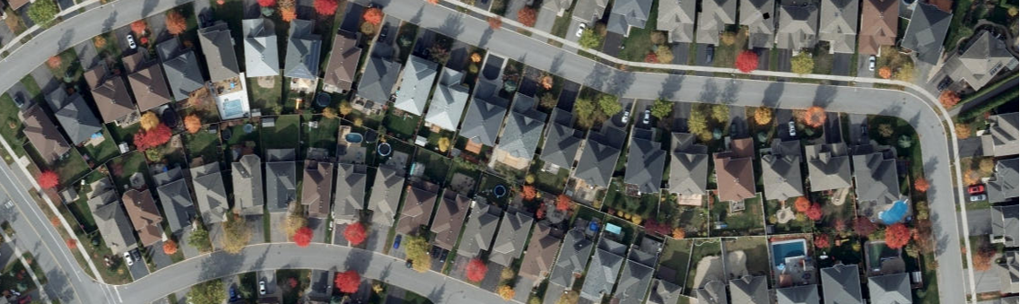 Vue à vol d’oiseau d’un quartier de banlieue ponctué de rangées de maisons et d’arbres lisérant les rues