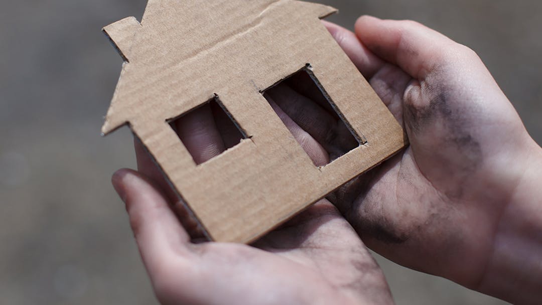 Hands holding a cardboard cutout of a house.