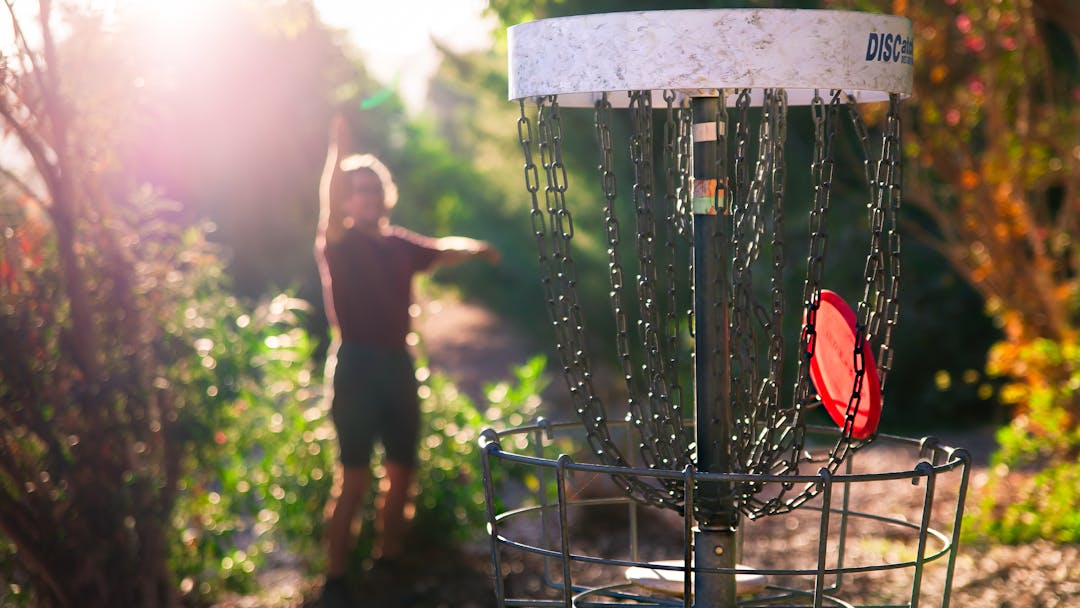 Person throws disc into basket on sunny day in the park
